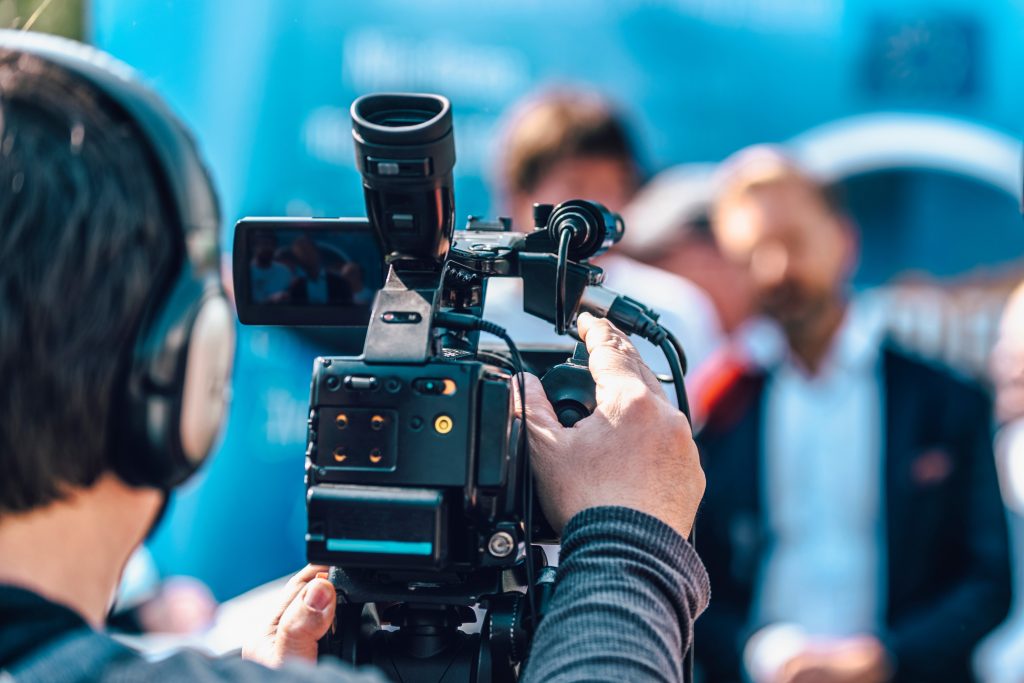 cameraman at an outdoor media event. blurred speaker in the back