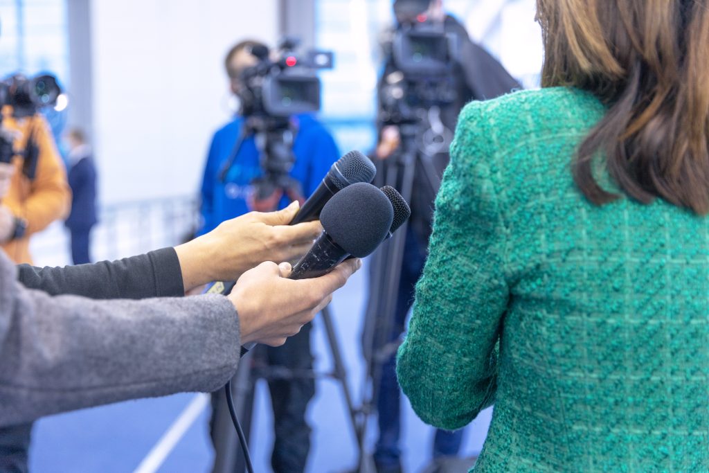 journalists at news conference holding microphones making media interview with female politician or business woman
