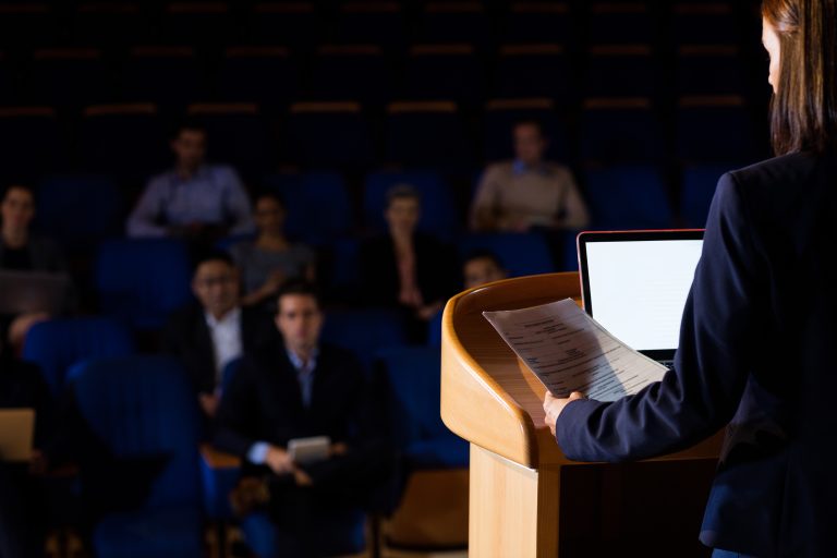 rear view of female business executive giving a speech at conference center